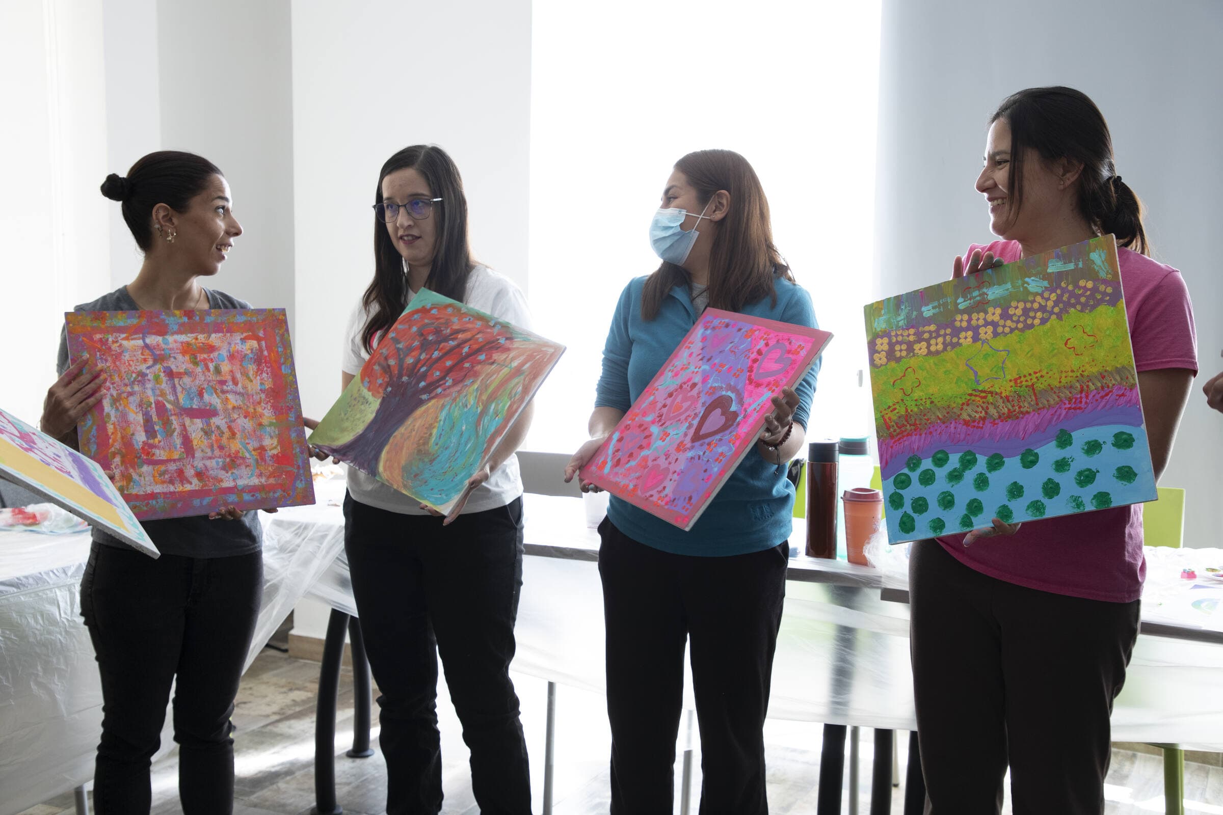 Cuatro participantes de pie mostrándose entre ellas los cuadros que terminaron de pintar.