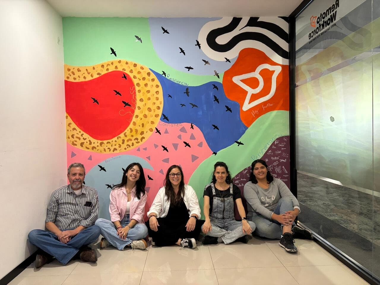 Equipo de una empresa sentado frente al mural que pintaron juntos en su taller con Mirari.